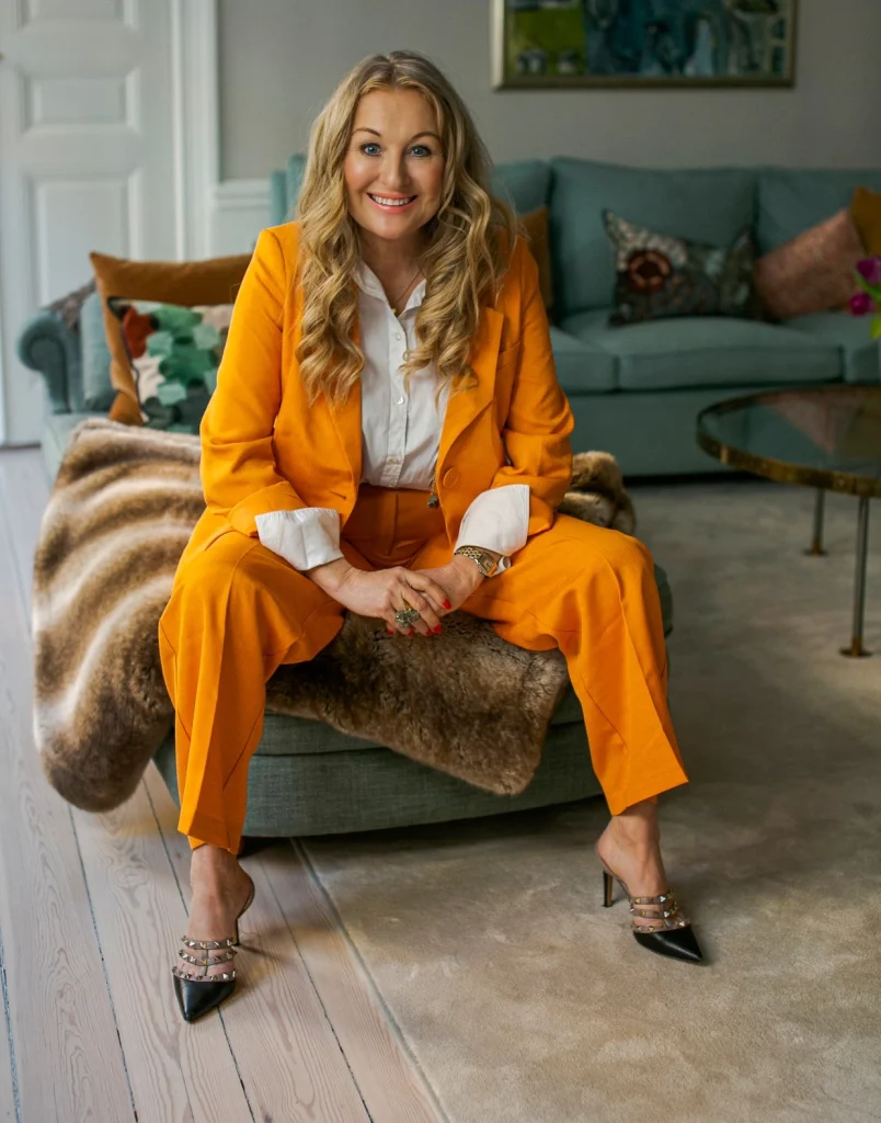 Jessica MacDowall i en vardagsrumssoffa med orange kavaj