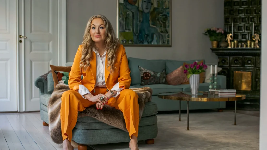 Jessica MacDowall sittande i ett vardagsrum med orange kostym